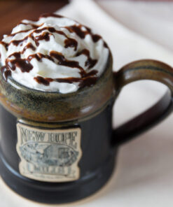 Photo of drink with whipped cream and chocolate syrup drizzle in a black pottery mug