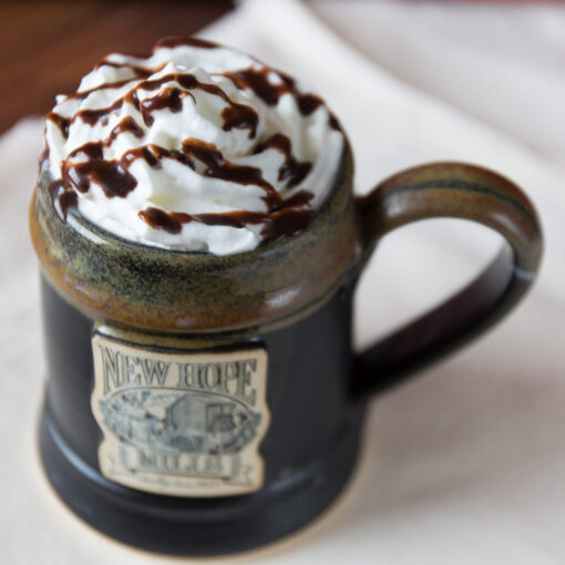 Photo of drink with whipped cream and chocolate syrup drizzle in a black pottery mug