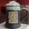 Photo of large New Hope Mills logo pottery mug with whipped cream protruding from the top; black with white glaze