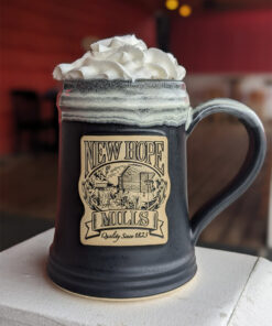 Photo of large New Hope Mills logo pottery mug with whipped cream protruding from the top; black with white glaze
