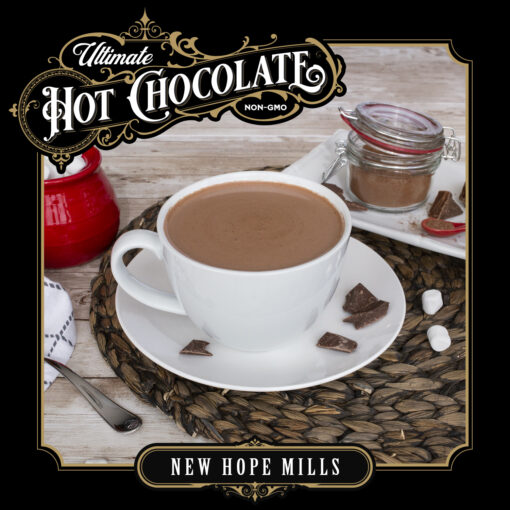 An image showing prepared Ultimate Hot Chocolate in a mug, with bits of chocolate, marshmallows, and kitchenware around the mug. Image contains text "Ultimate Hot Chocolate (NON-GMO). New Hope Mills.