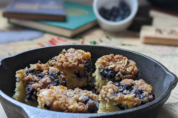 Photo of Blueberry Buckle Cake in a small skillet, with décor in the background.